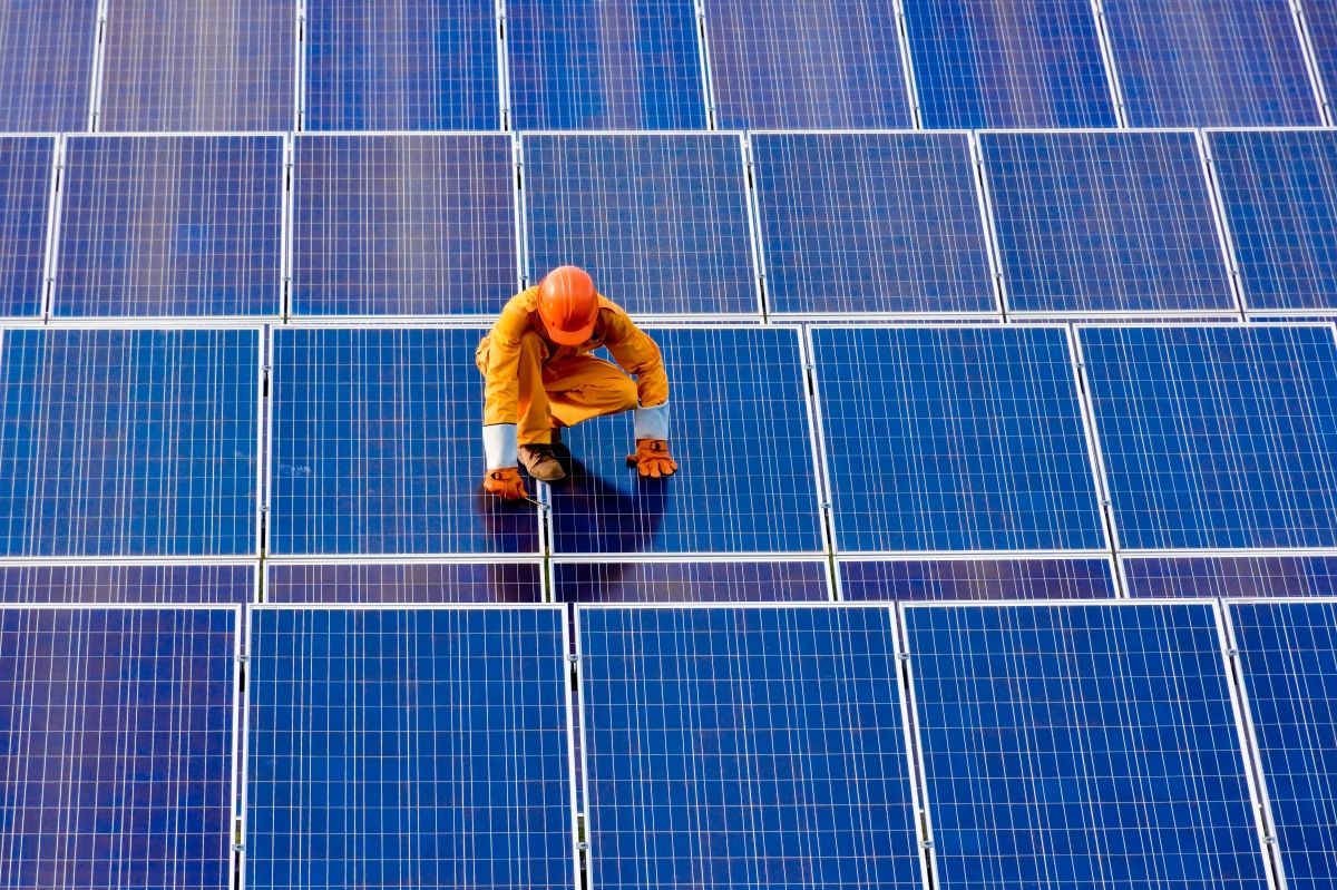 Un hombre está arrodillado encima de un panel solar.