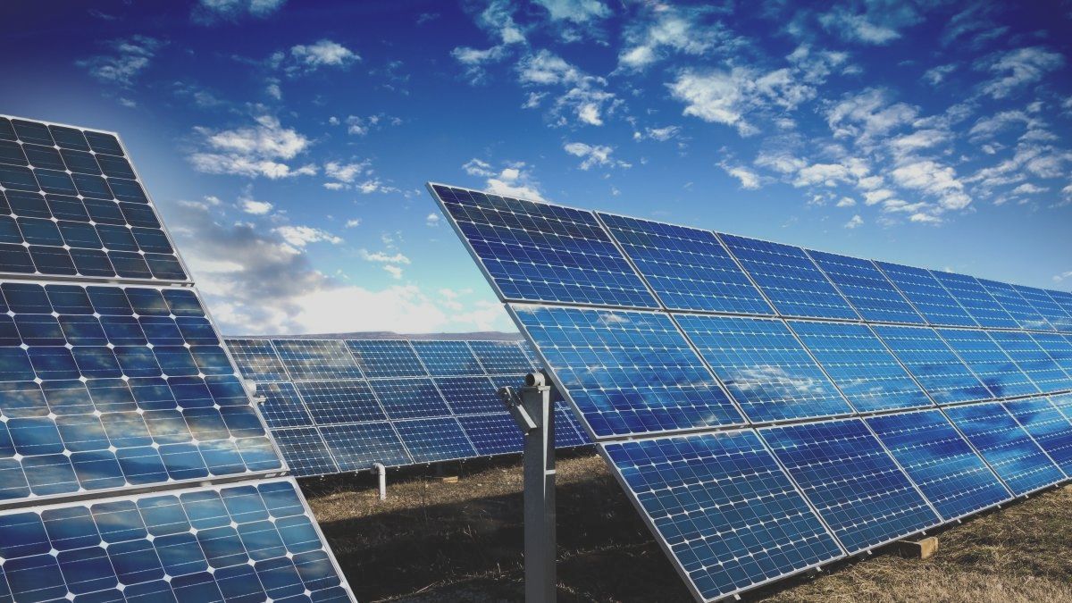 Una fila de paneles solares contra un cielo azul con nubes.