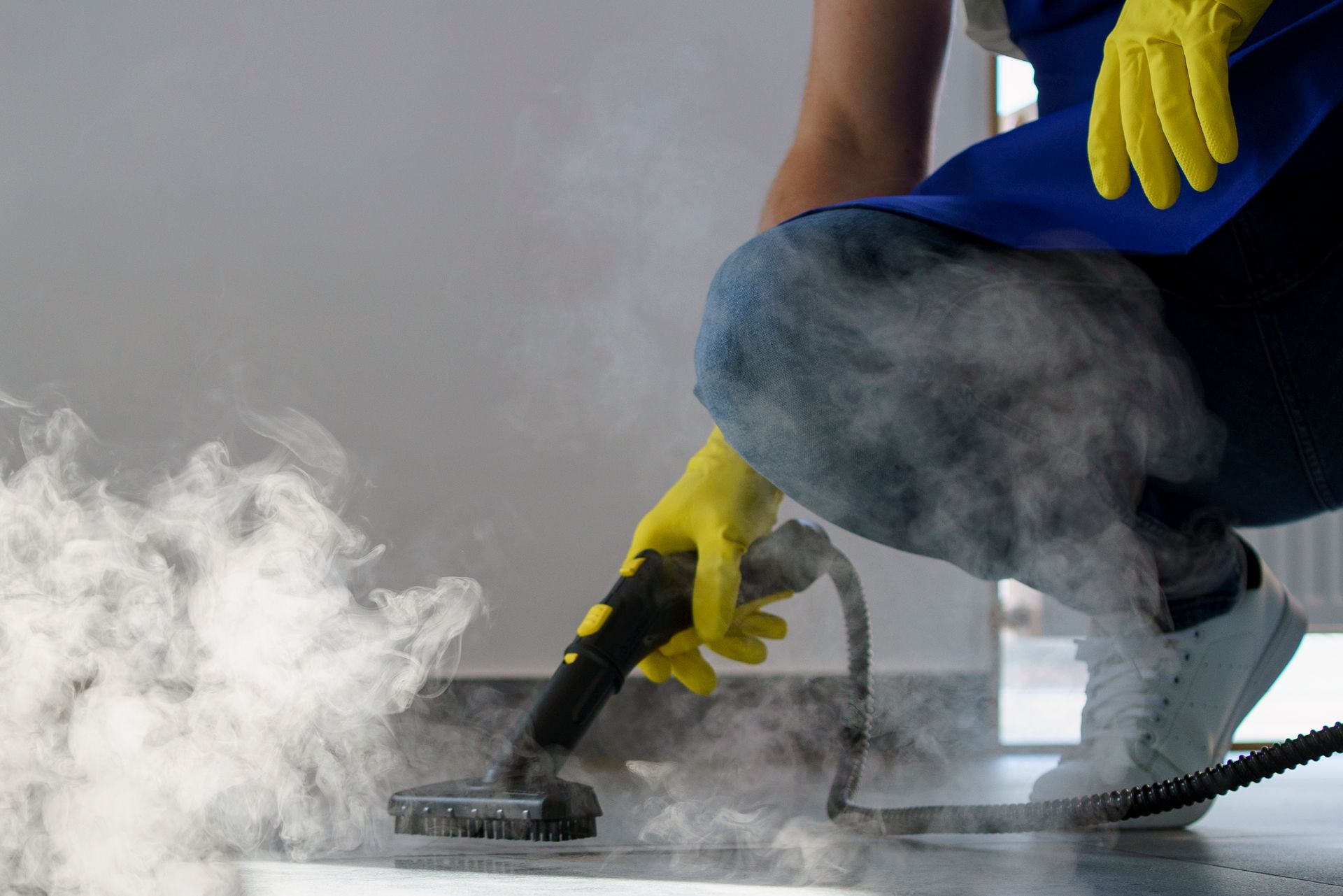 Una persona que lleva guantes amarillos está usando un limpiador a vapor para limpiar un piso.