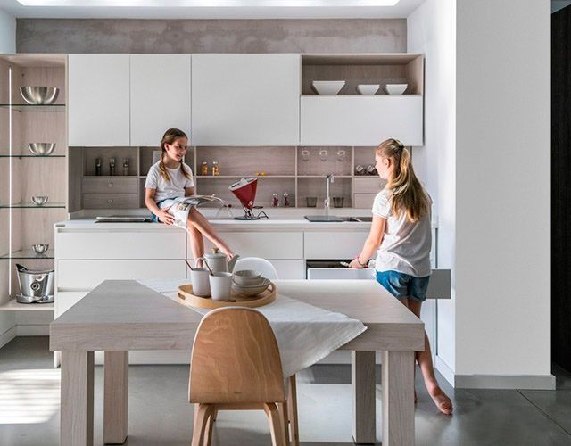 Dos chicas están sentadas en una mesa en una cocina.