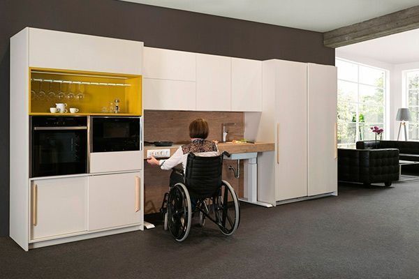Una persona en silla de ruedas está sentada en un escritorio en una cocina.