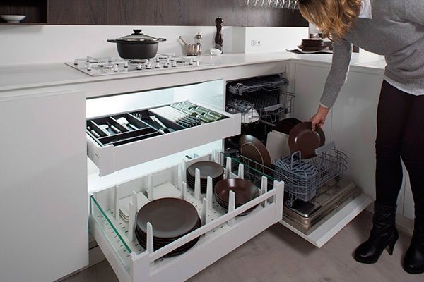 Una mujer mete la mano en un cajón de la cocina lleno de platos y ollas.