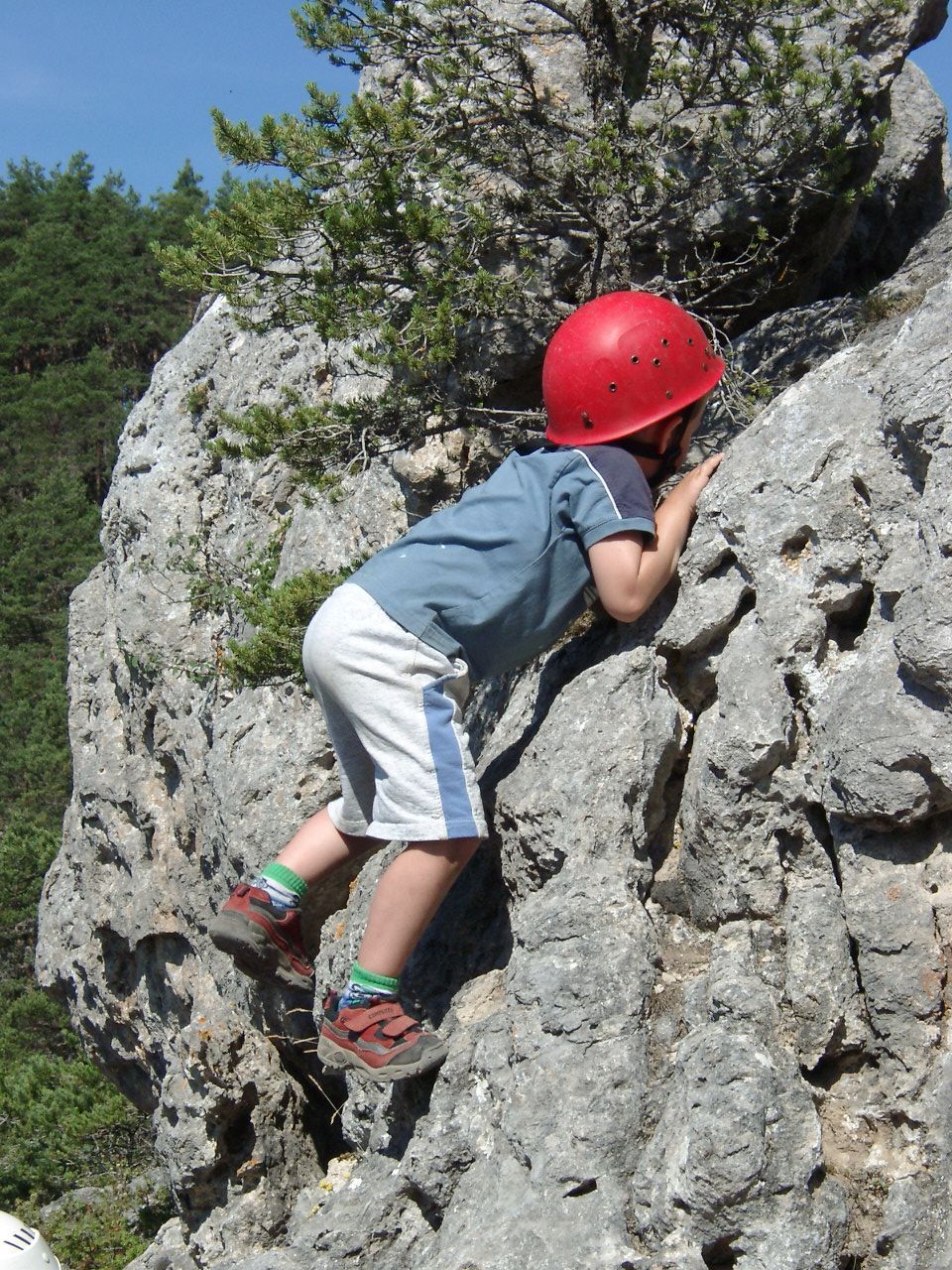 Enfant portant un casque rouge escaladant une falaise rocheuse par une journée ensoleillée