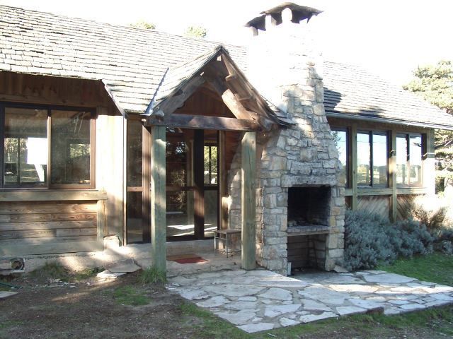 Entrée d'une maison en pierre avec porche en bois, fenêtres et petit chemin d'accès à l'avant, baignée de lumière naturelle.