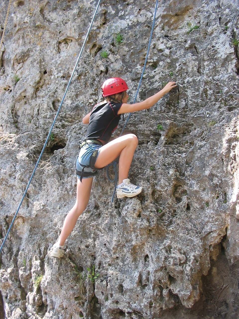 Un grimpeur casqué escalade une falaise grise abrupte à l'aide d'une corde.
