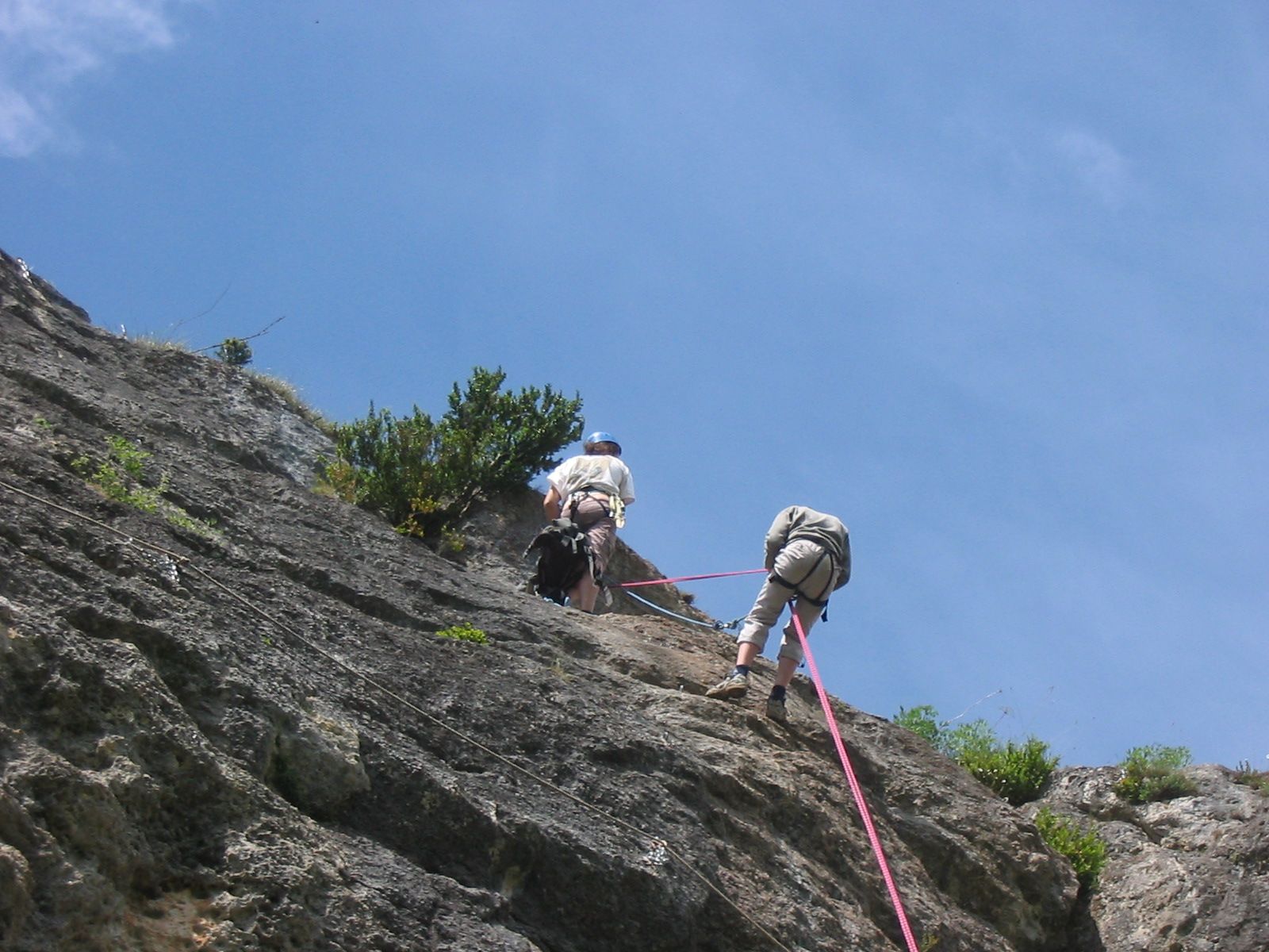 Deux alpinistes encordés sur une falaise rocheuse abrupte sous un ciel bleu lors d'une ascension