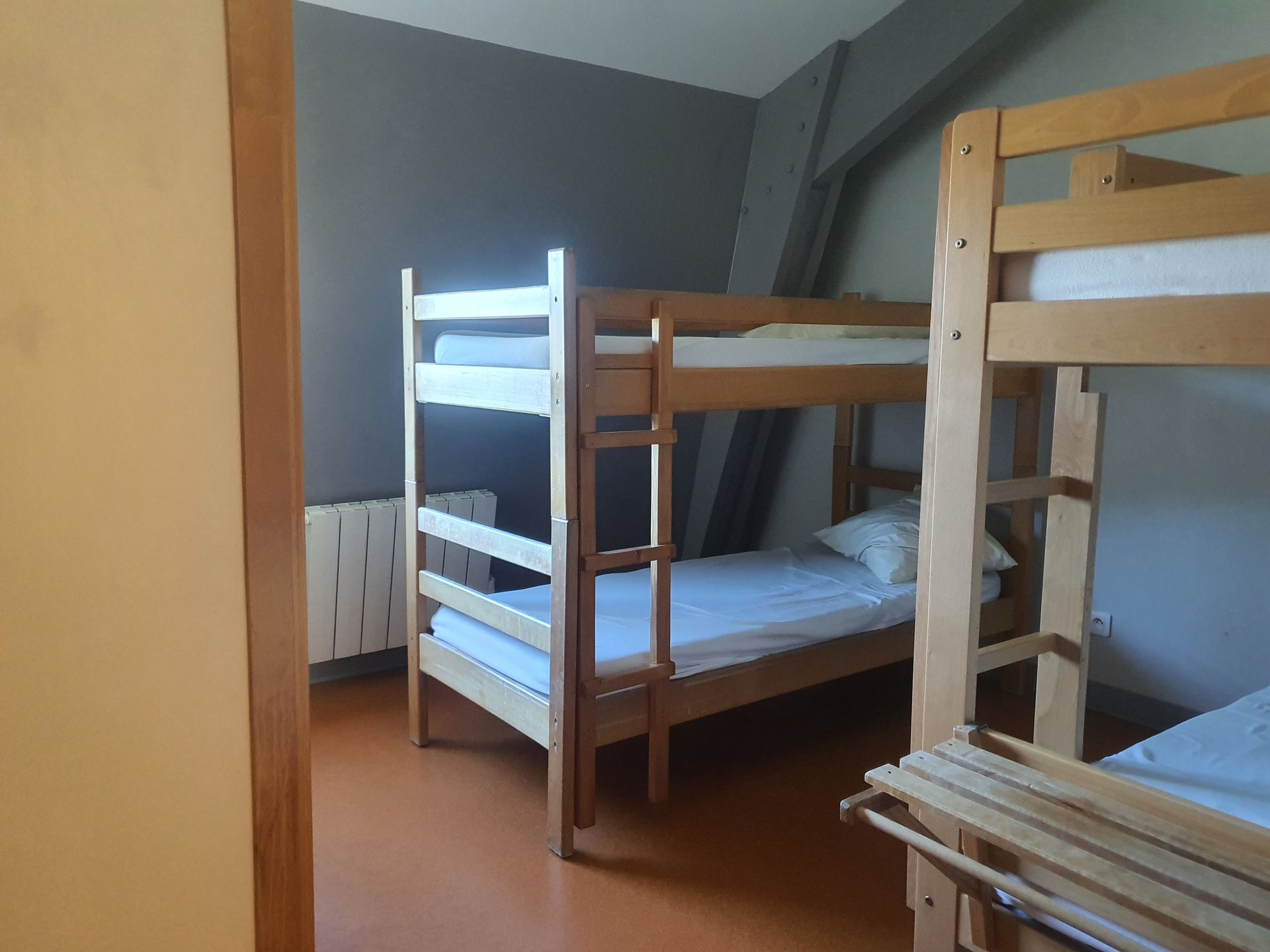 Chambre de dortoir avec deux lits superposés en bois et un petit radiateur mural.