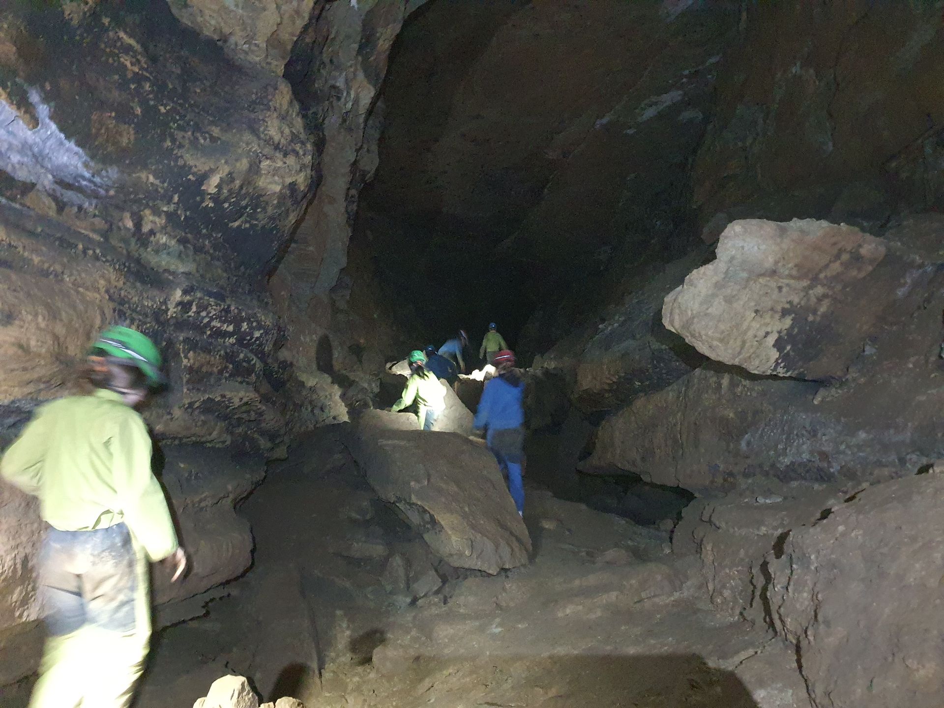 Des personnes casquées explorent une grotte rocheuse sombre à l'aide de lampes frontales.