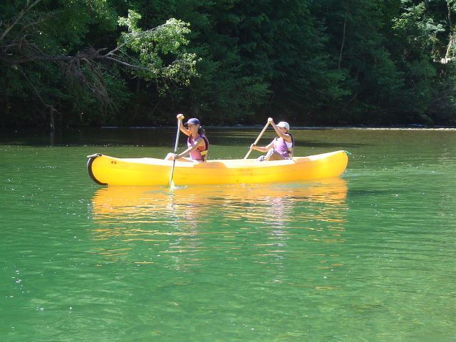 Deux personnes pagayant en kayak jaune sur une eau verte près d'une rive boisée
