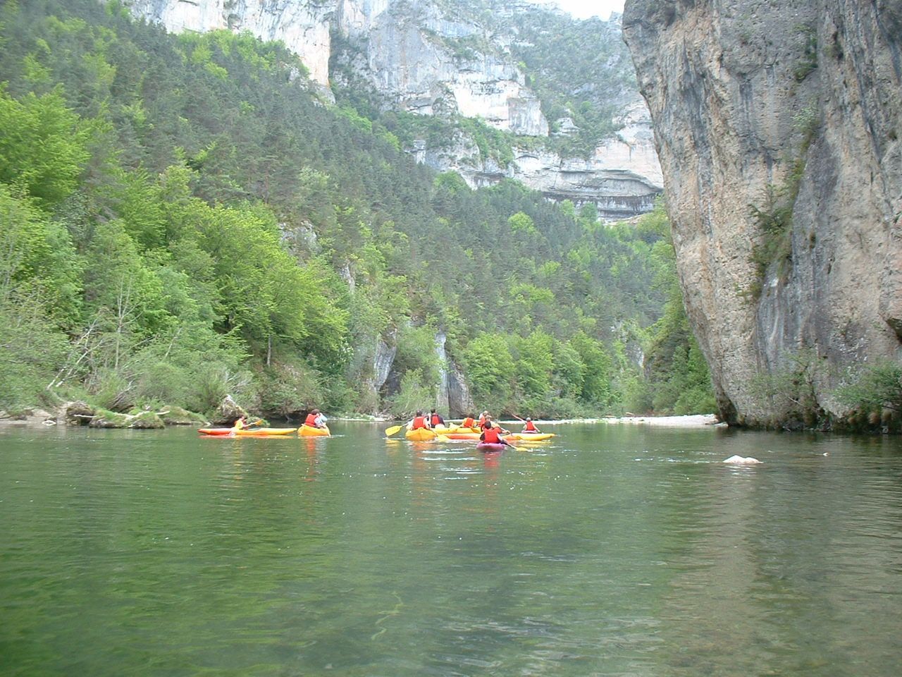 Des kayakistes pagayent sur une rivière calme entre des falaises verdoyantes et une gorge rocheuse