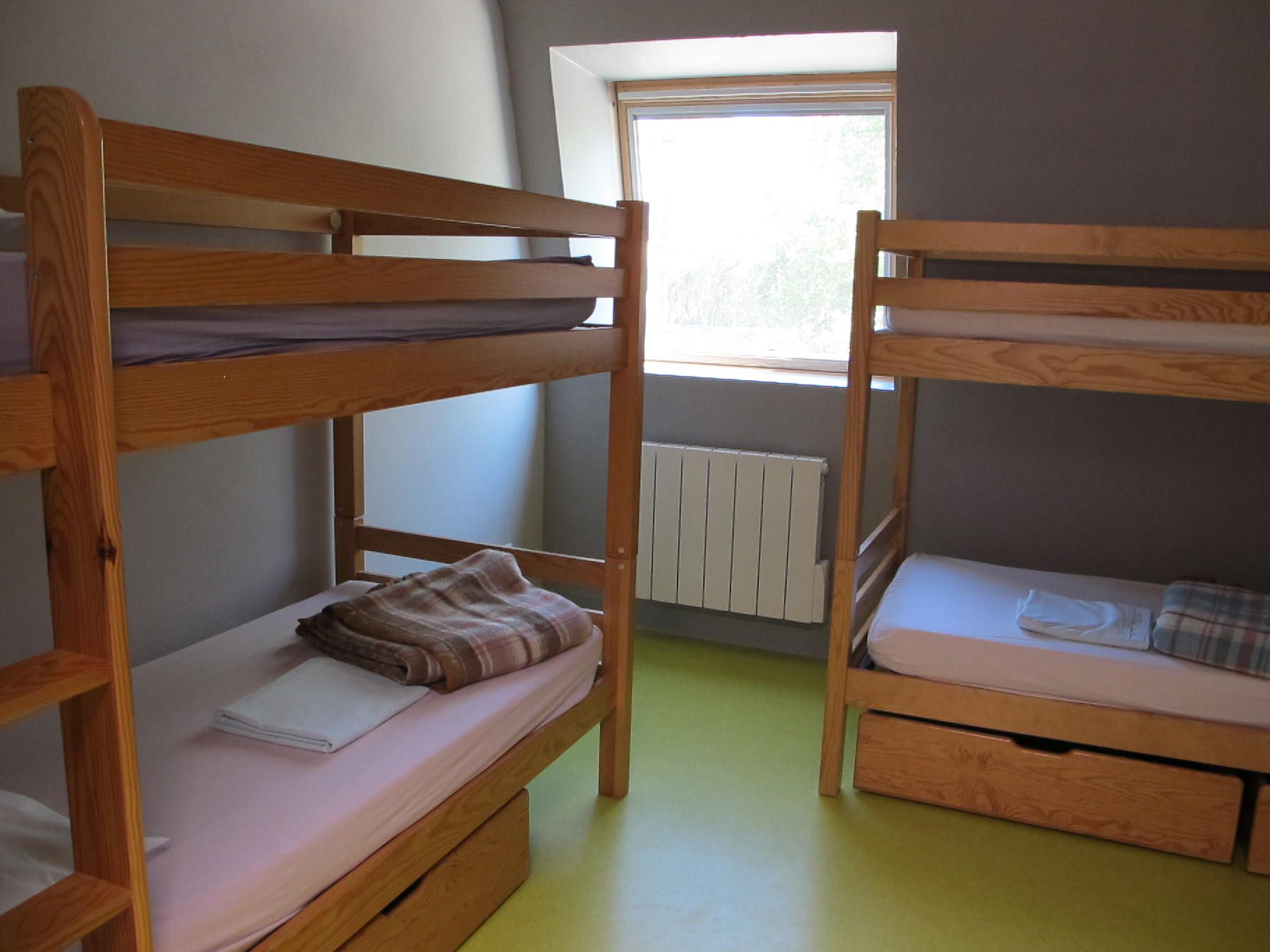 Petite chambre avec deux lits superposés en bois, une fenêtre, un radiateur et un sol vert.