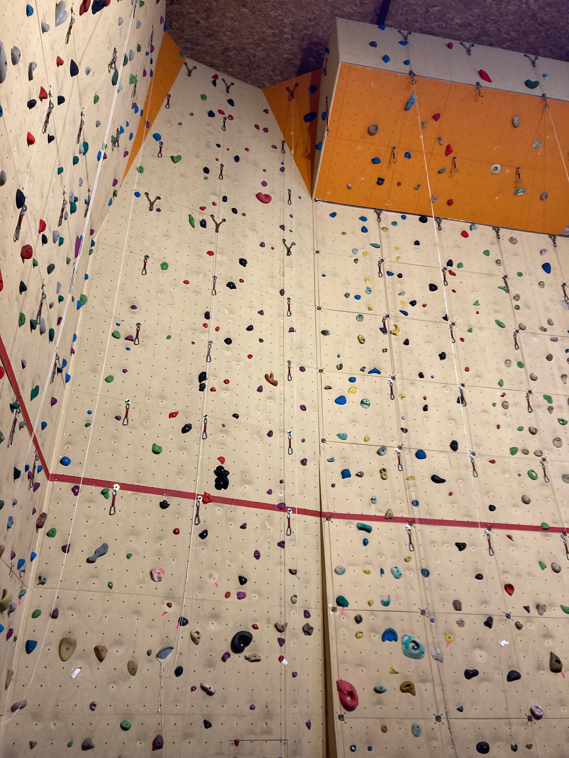 Mur d'escalade intérieur avec prises multicolores et surplombs orange.
