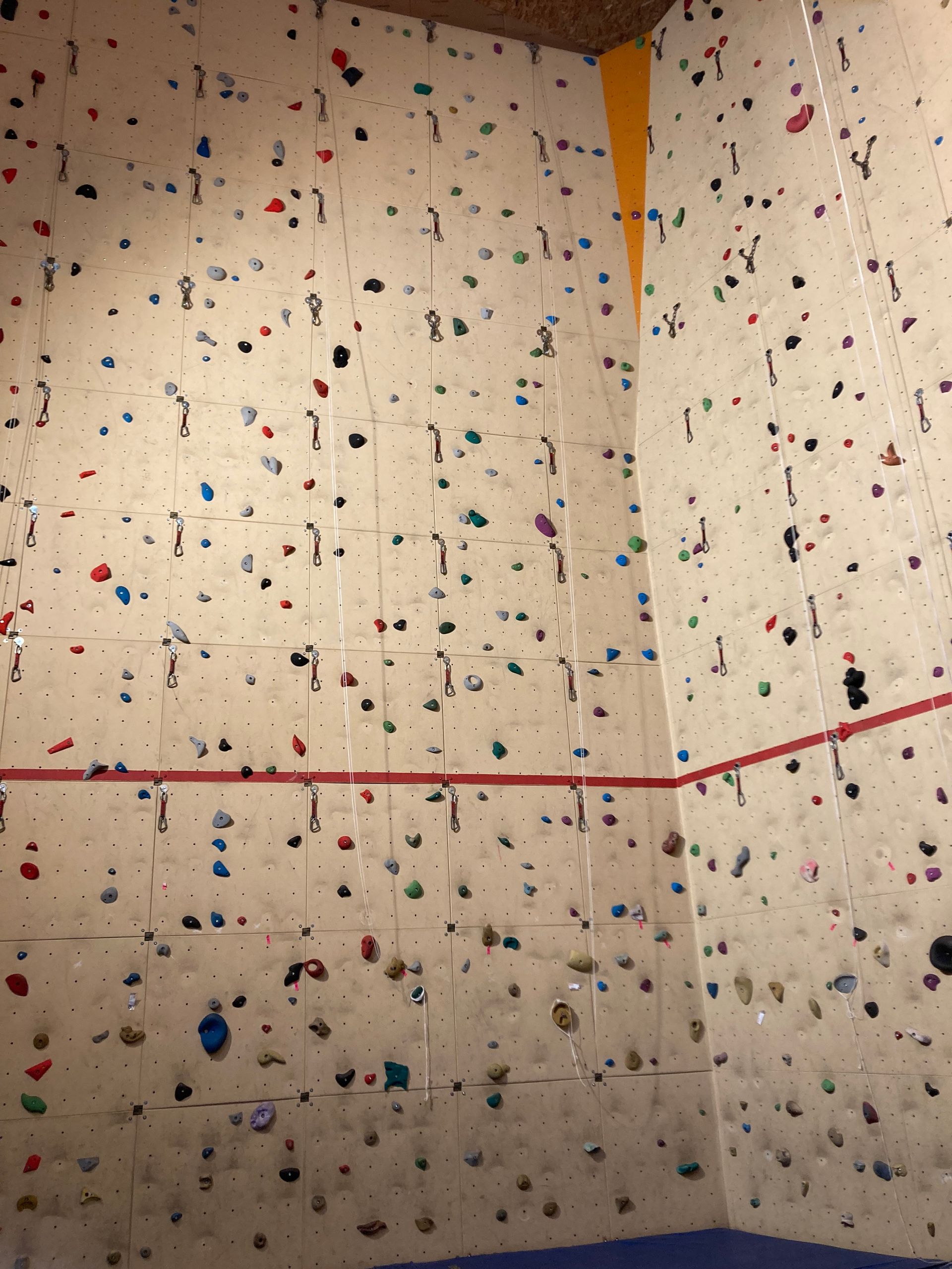 Mur d'escalade intérieur avec prises multicolores et une ligne horizontale rouge.