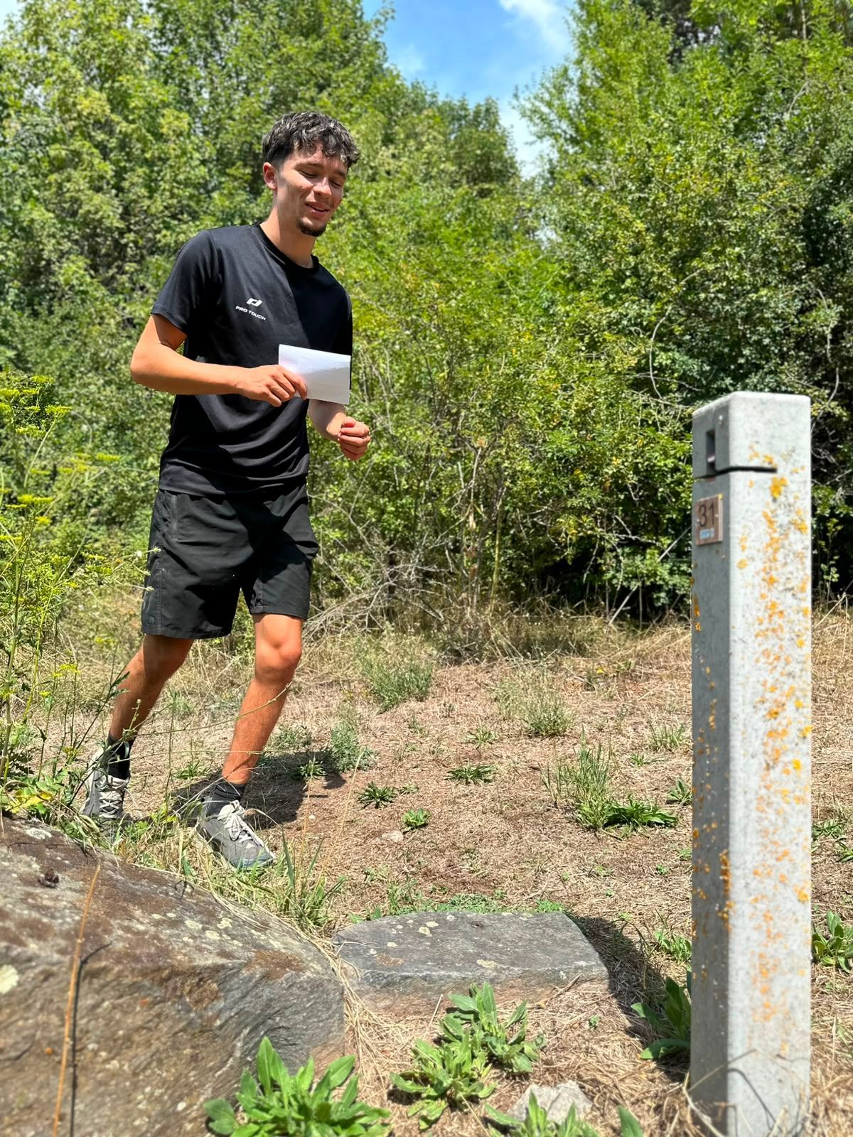 Une personne en tenue de sport noire court à l'extérieur, près d'arbres et d'un poteau blanc.