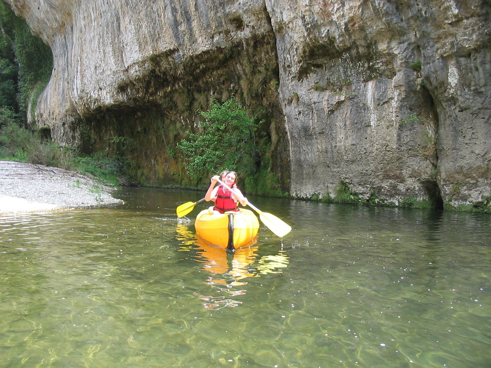 Une personne dans un kayak jaune sur une eau verte et calme, près d'une paroi rocheuse de grotte.