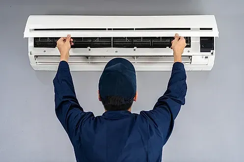 Un hombre está arreglando un acondicionador de aire en una pared.