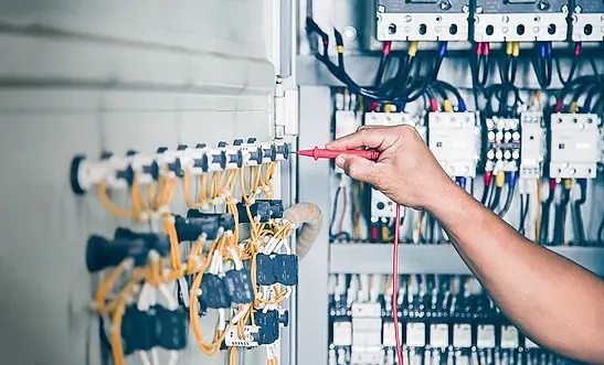 Una persona está trabajando en un panel eléctrico con un destornillador.