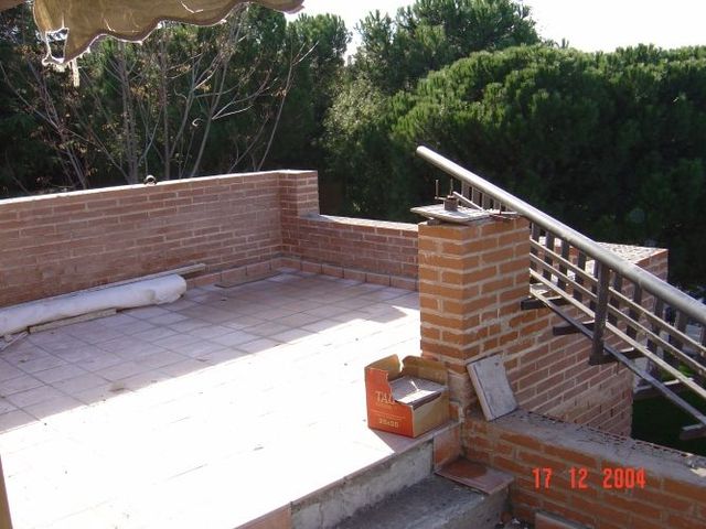 Un balcón de ladrillo con escaleras y árboles al fondo.