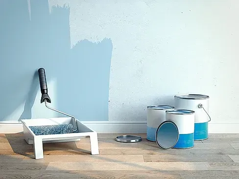 Se está pintando una pared con un rodillo y baldes de pintura.
