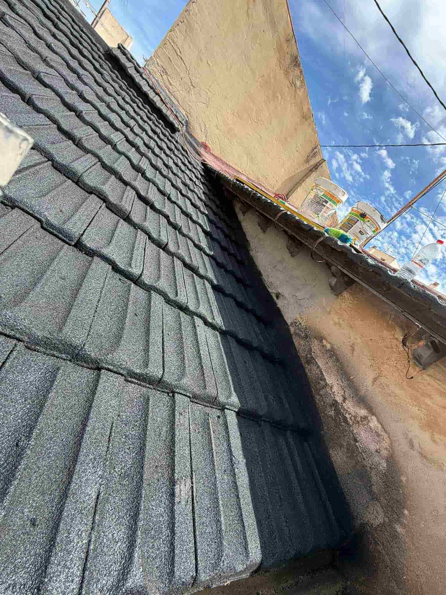 Una vista de ángulo bajo de un techo gris texturizado con una pared de color claro bajo un cielo azul brillante.