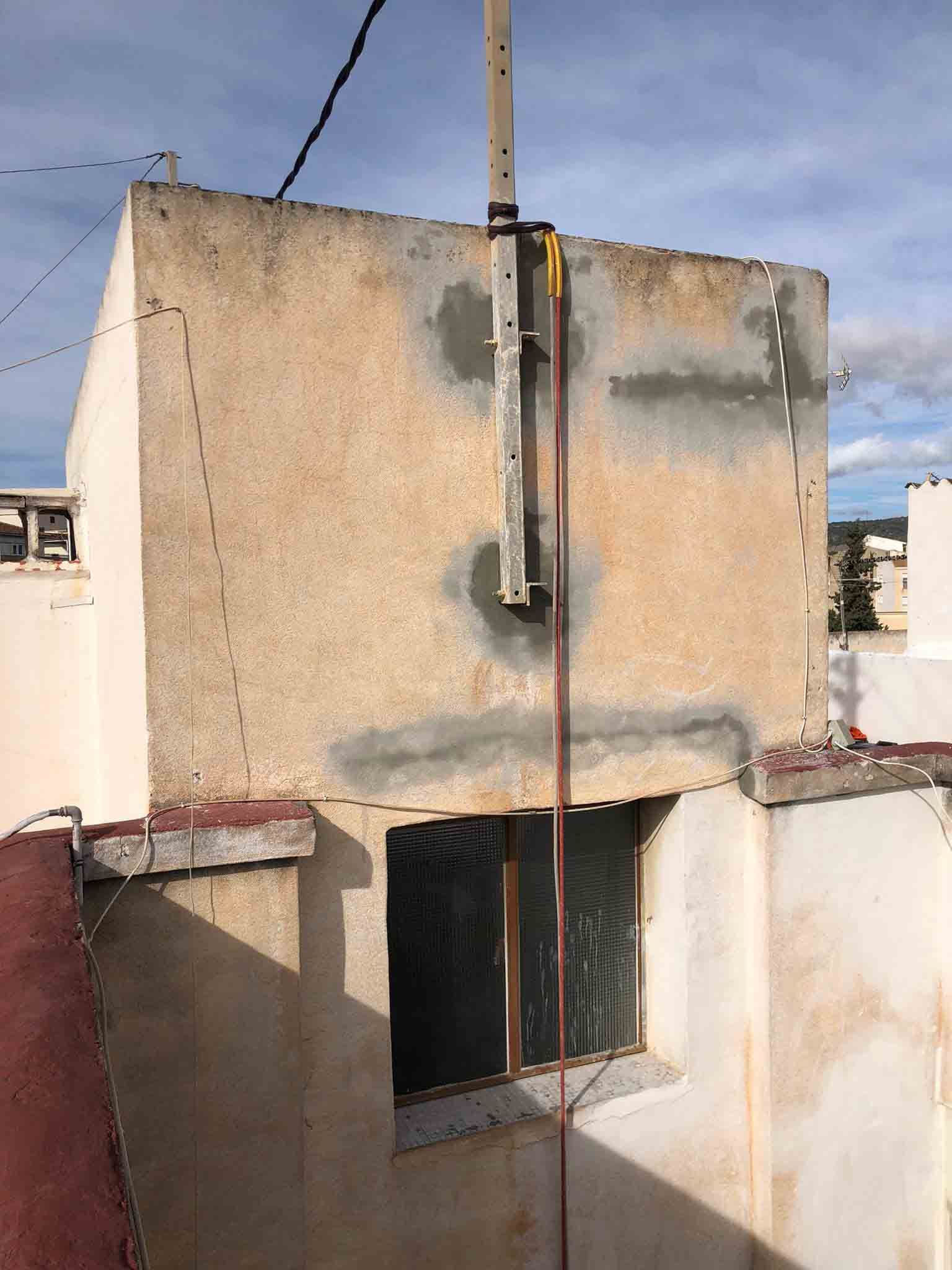 Edificio de hormigón con ventana, poste eléctrico y cables contra un cielo nublado.