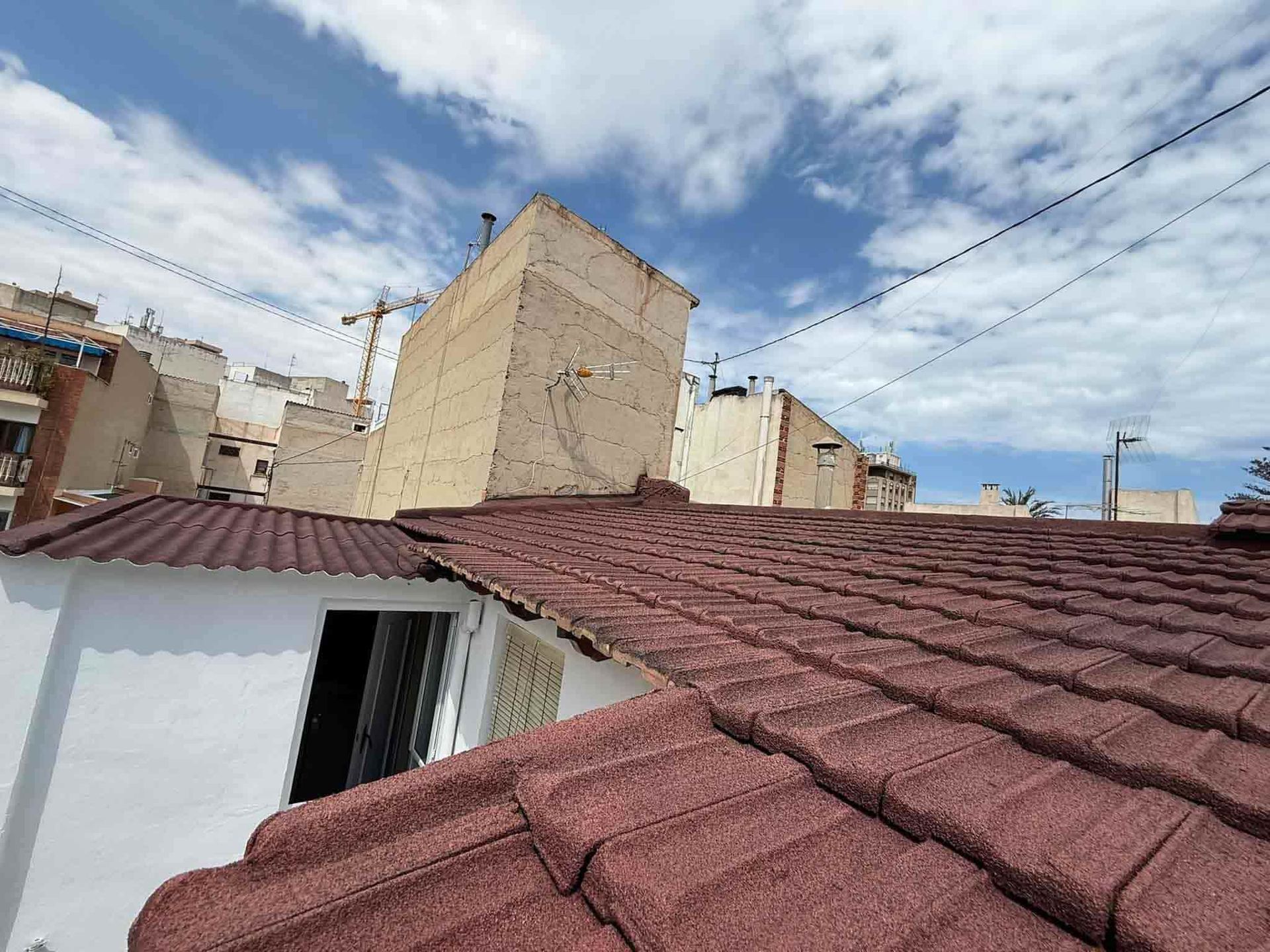 Techo de tejas rojas con edificios y un cielo azul con nubes al fondo.