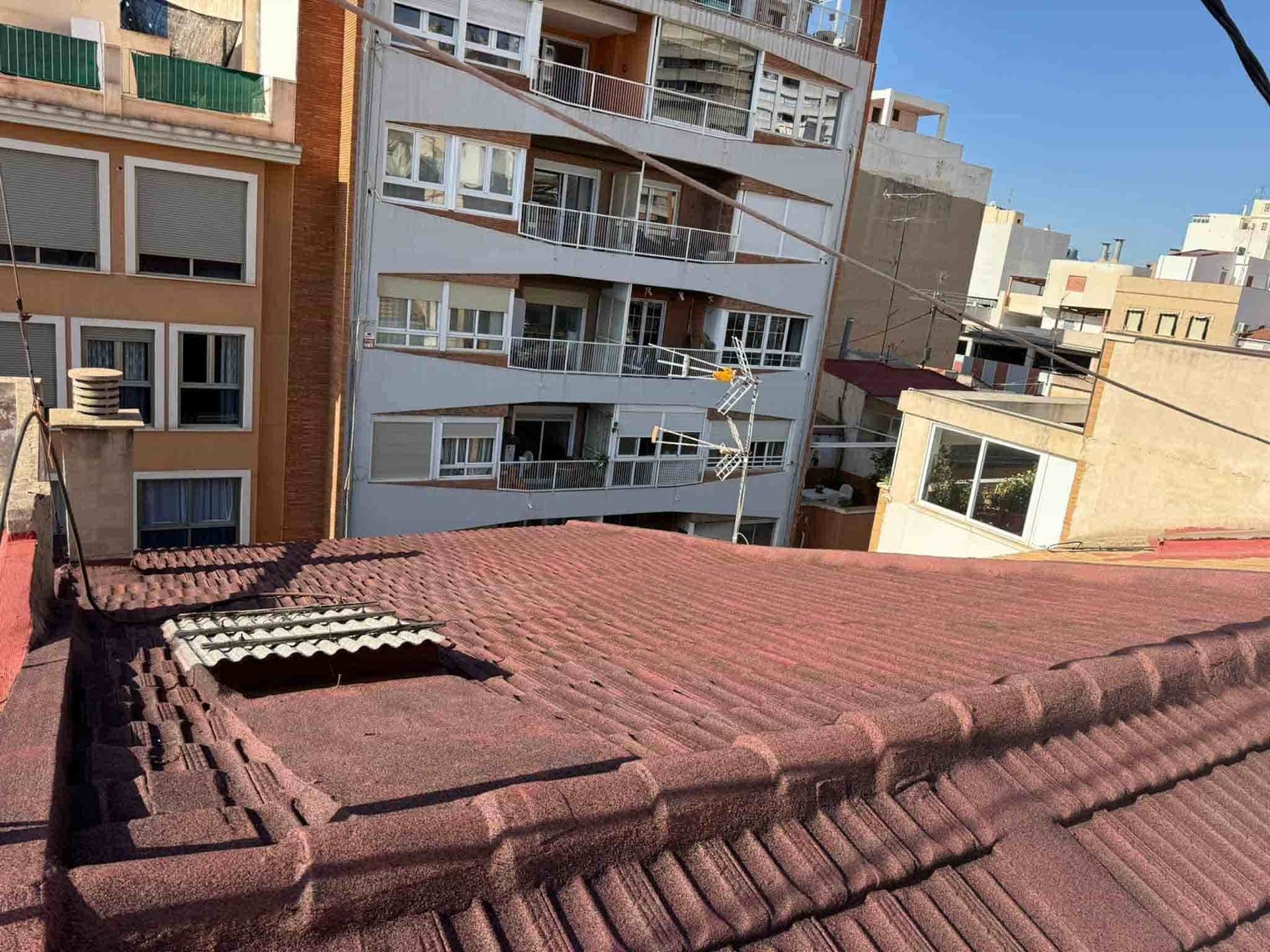 Tejado de tejas rojas con edificios al fondo, cielo azul.