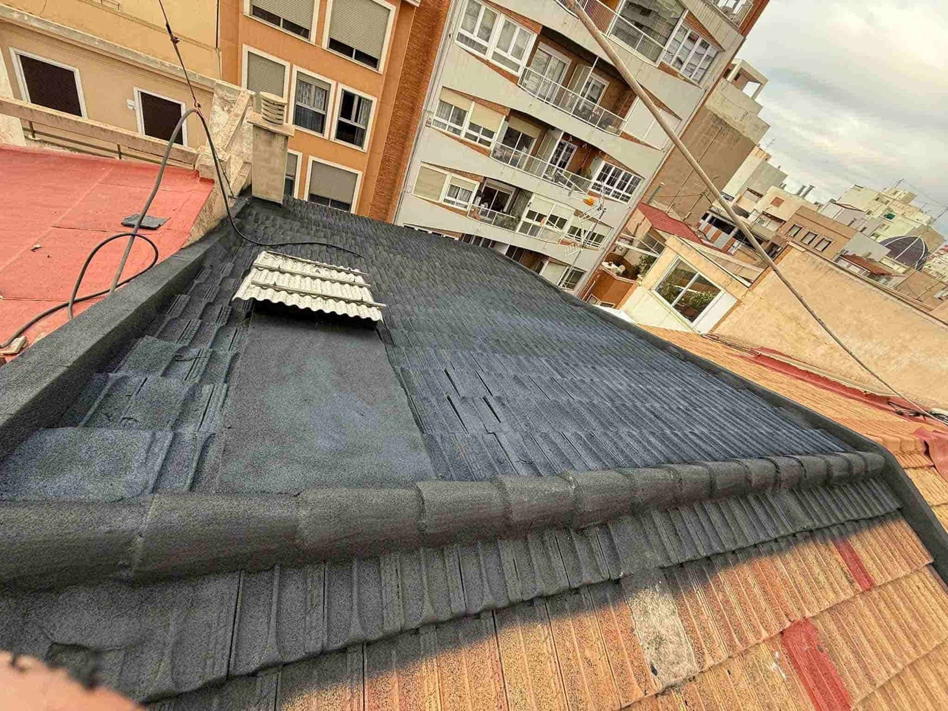 Vista de un techo plano con material de techado oscuro y un edificio al fondo.