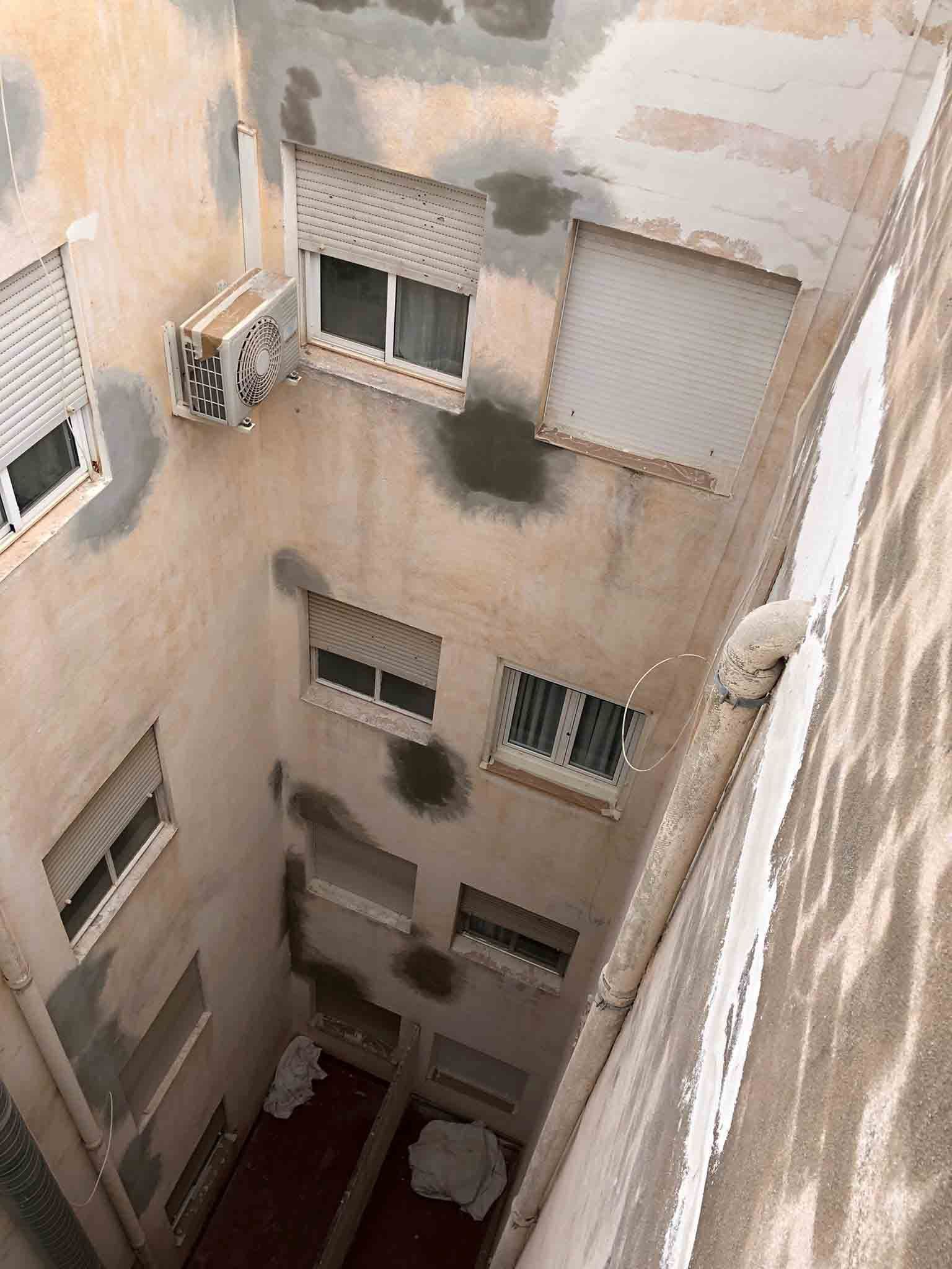 Vista exterior estrecha del edificio; varios pisos con ventanas, contraventanas y parches de pared reparados.