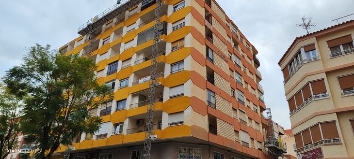 Azotea con tejas rojas contra un cielo azul brillante con nubes dispersas; se ven líneas eléctricas y un edificio.