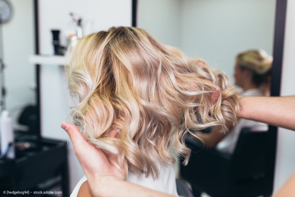 Blondes Haar, das im Salon in lockeren Locken gestylt wurde und von den Händen der Stylistin gehalten wird.