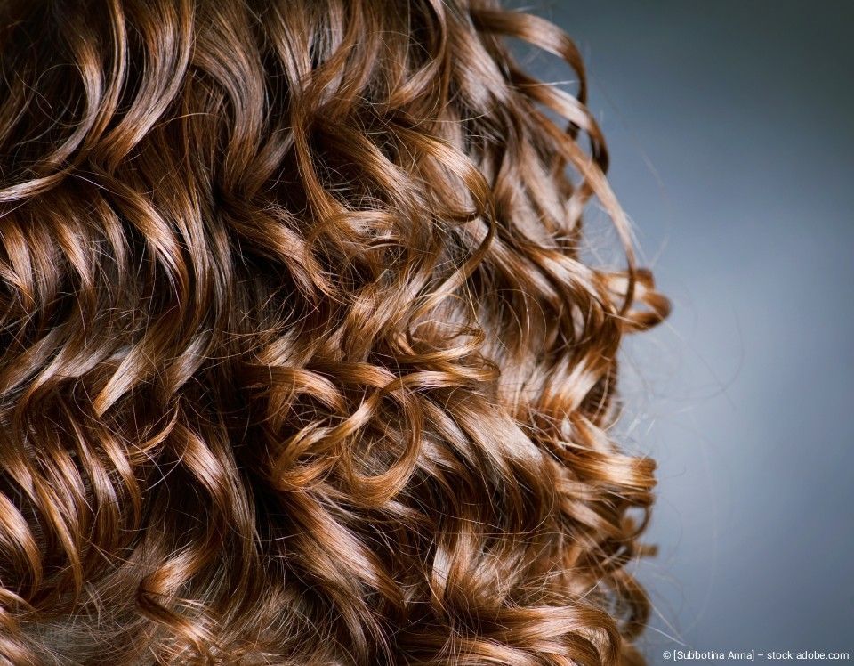 Nahaufnahme von braunem, lockigem Haar vor dunklem Hintergrund.