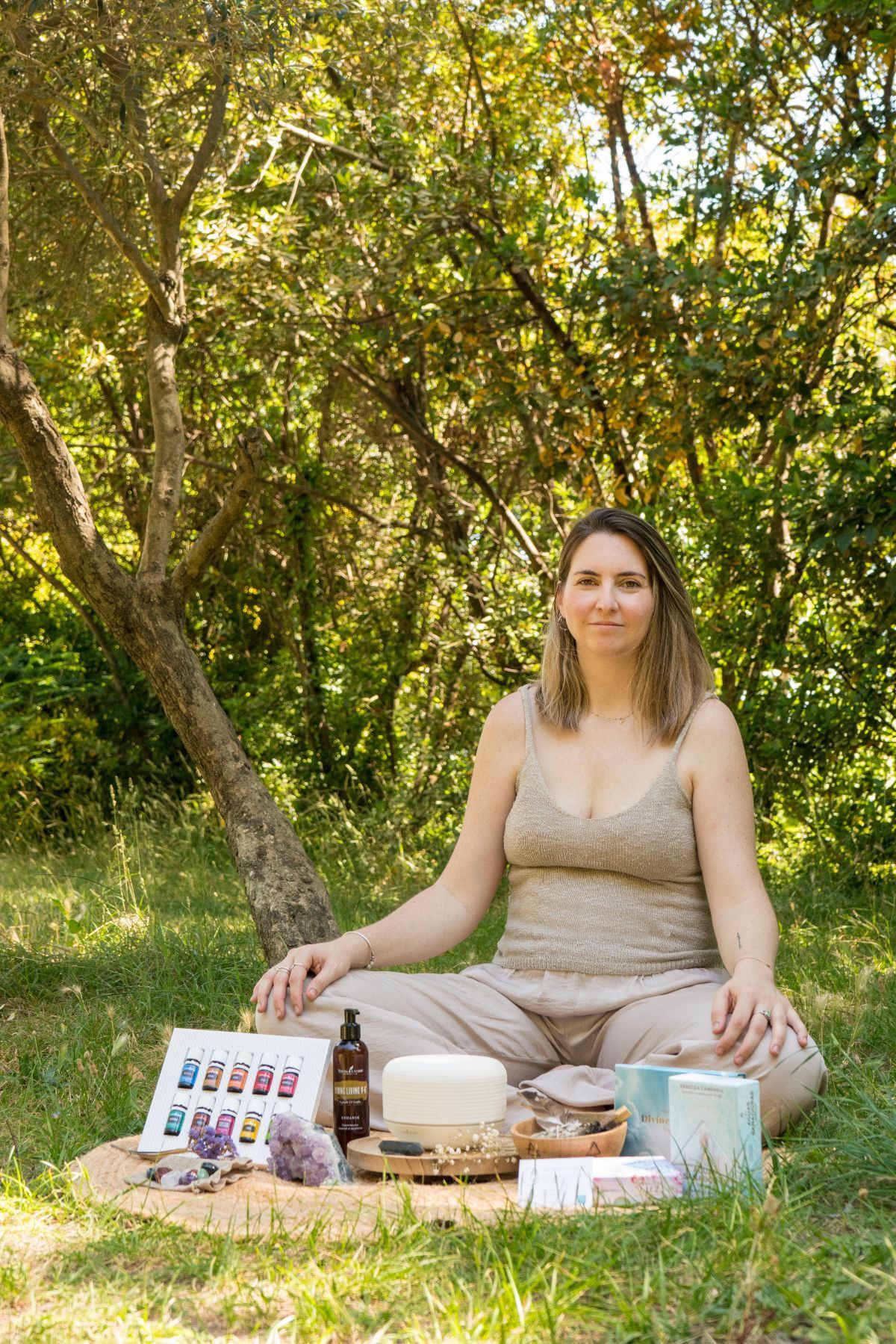 Mujer meditando al aire libre sobre una manta con un juego de té y libros, rodeada de árboles verdes.