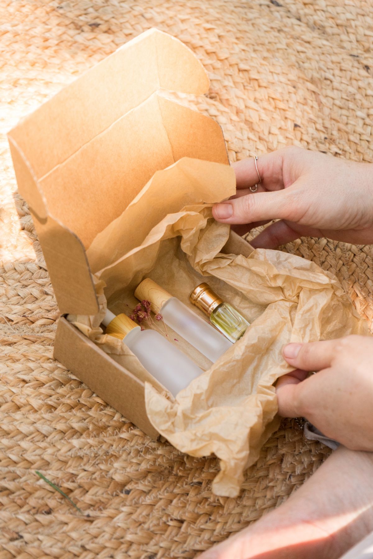 Manos abriendo una caja de frascos de productos para el cuidado de la piel sobre una estera tejida.