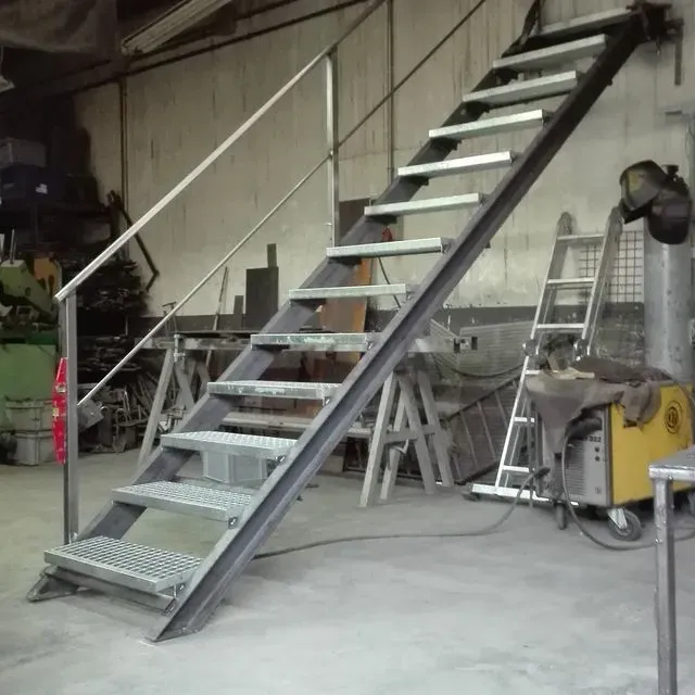 Una escalera de metal en un almacén con una máquina de soldar al fondo.