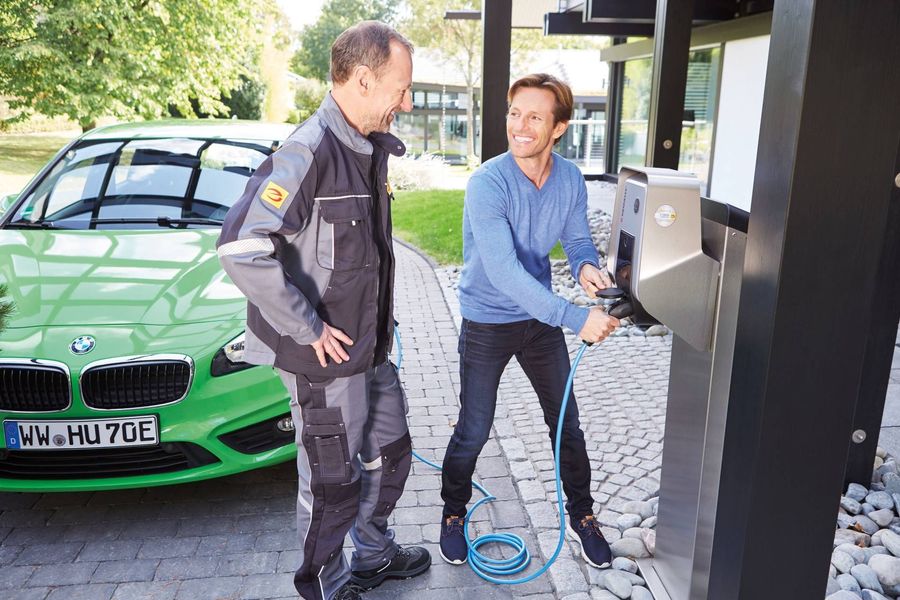 Zwei Männer stehen neben einem grünem Auto, einer bedient die E-Ladesäule