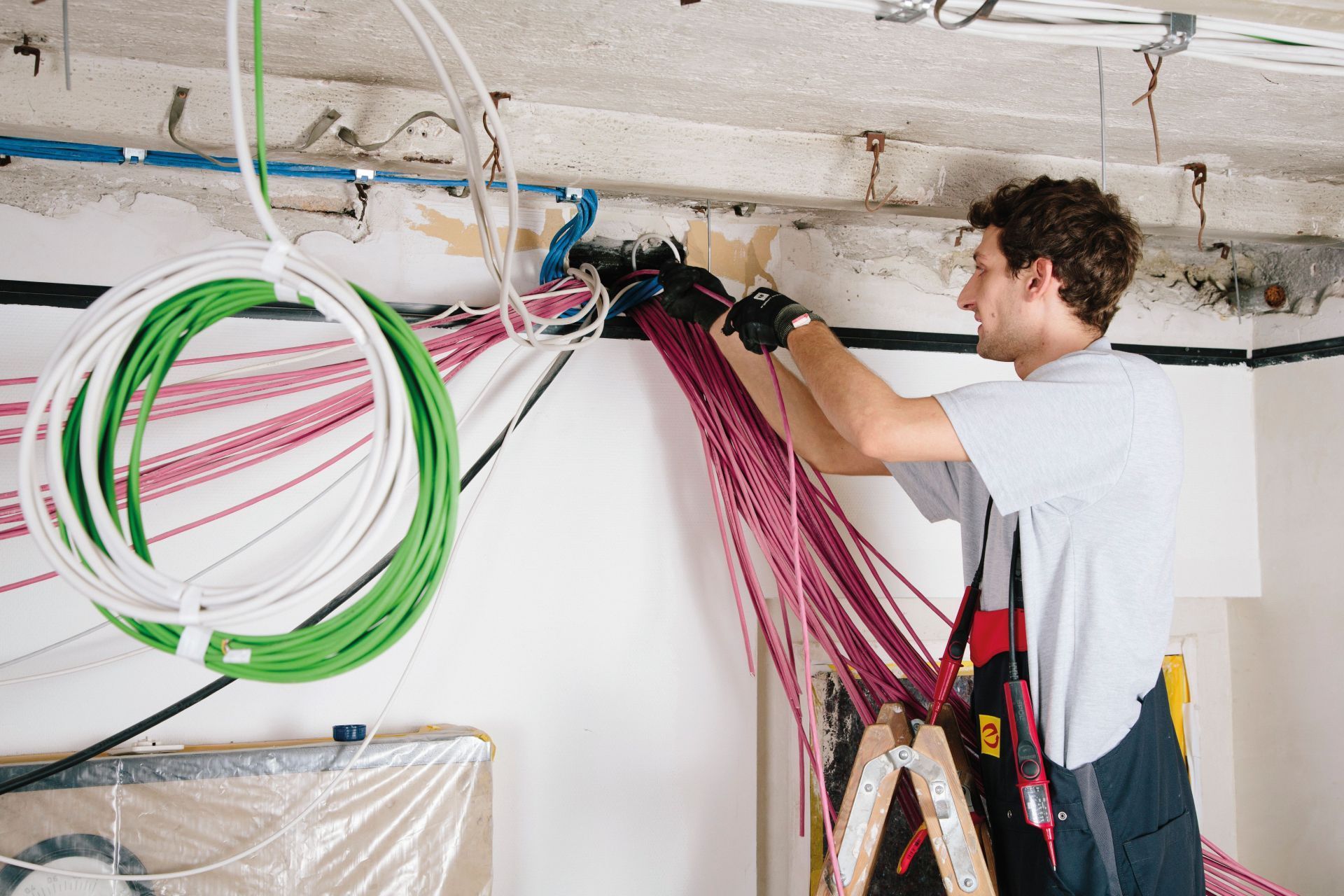 Elektriker arbeitet an Kabeln in unterschiedlichen Farben, die aus einer Wand kommen