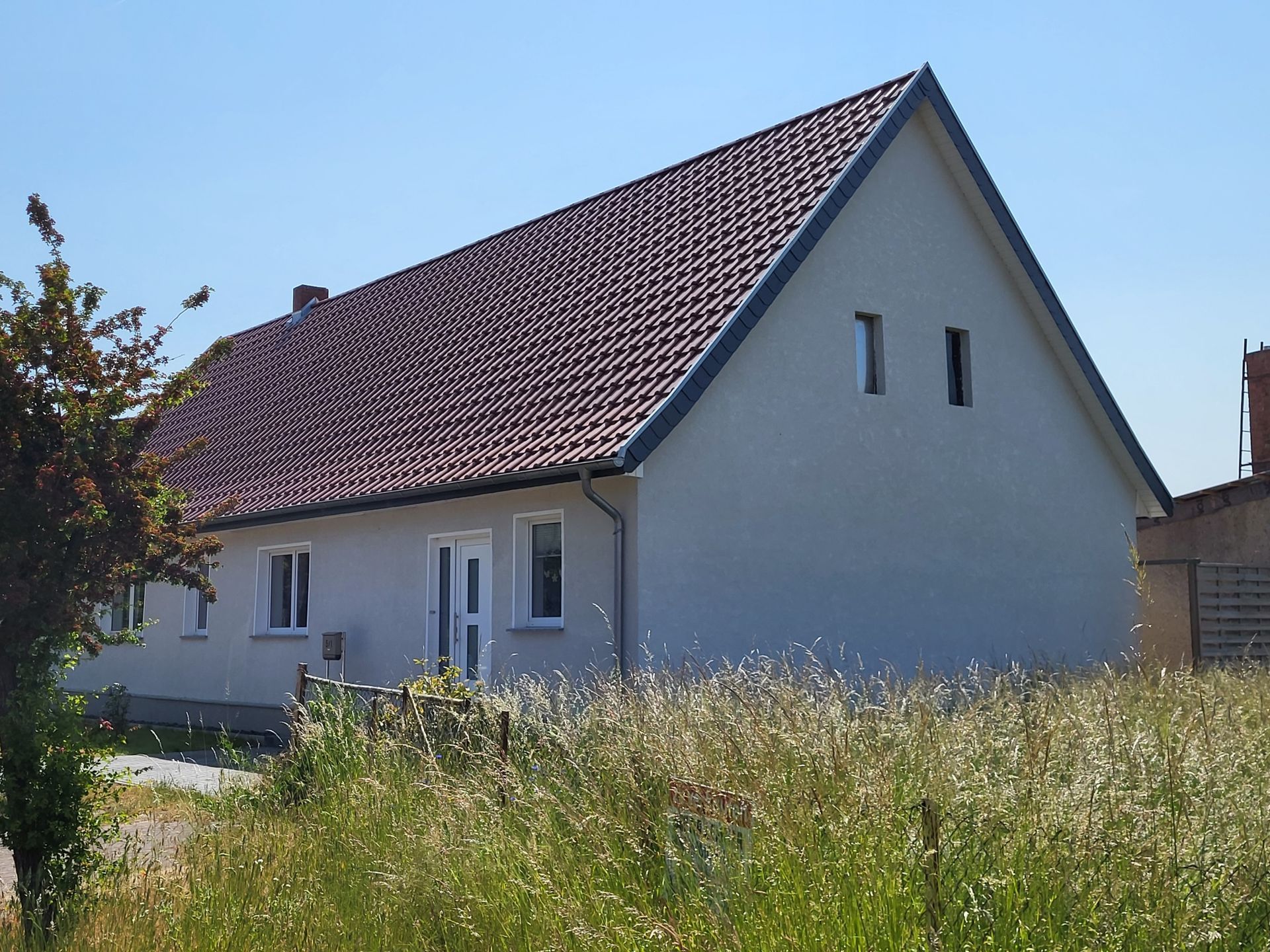 Ein weißes Haus mit einem roten Ziegeldach ist von hohem Gras umgeben