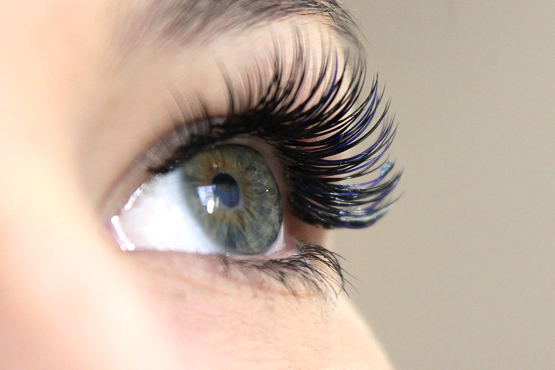 Primer plano de un ojo verde azulado con pestañas largas, oscuras y voluminosas, visto de perfil.