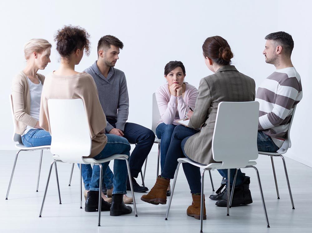 Personas sentadas en círculo, participando en una conversación; sala blanca, sillas.