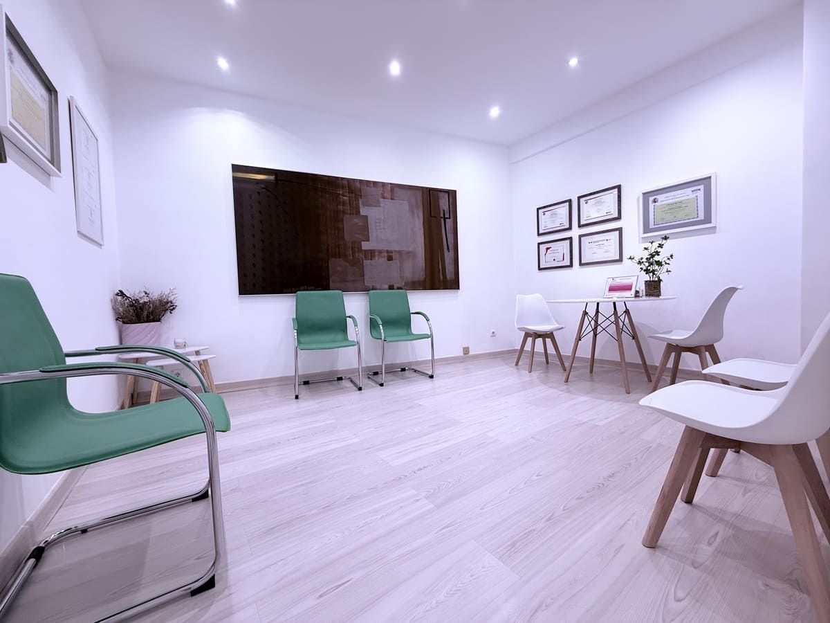 Sala de espera con sillas modernas, un televisor grande, diplomas y una mesita con flores.