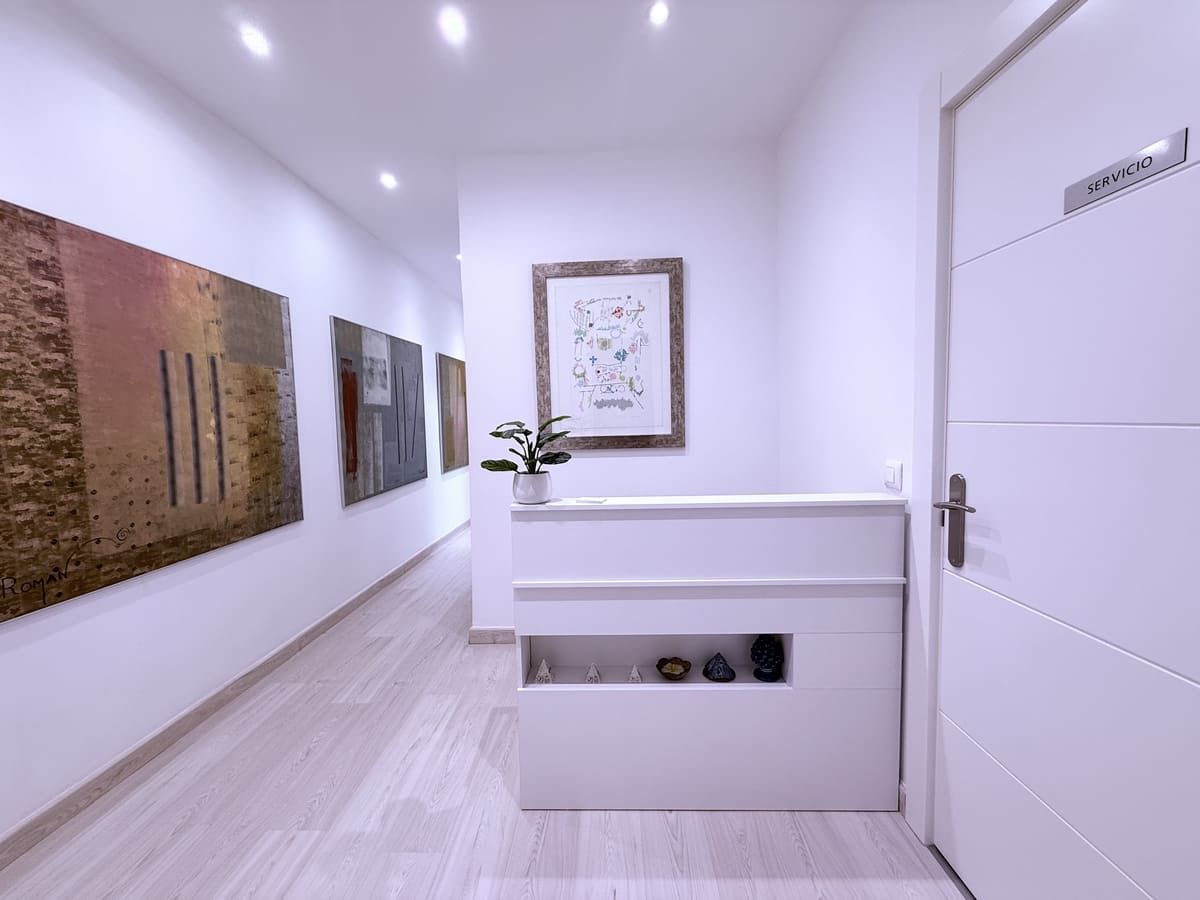 Pasillo con paredes blancas, cuadros y mostrador de recepción.