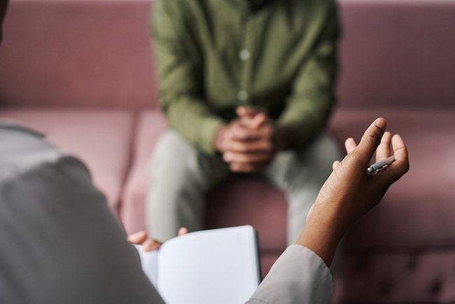 Terapeuta sosteniendo un bolígrafo, señalando a un paciente sentado en un diván rosa.