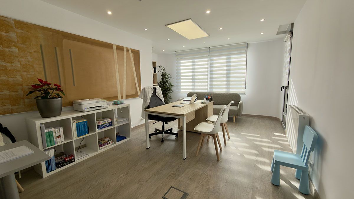 Espacio de oficina luminoso con una pared decorativa de madera, un mueble de almacenamiento blanco, un escritorio central, sillas y una pequeña silla azul.