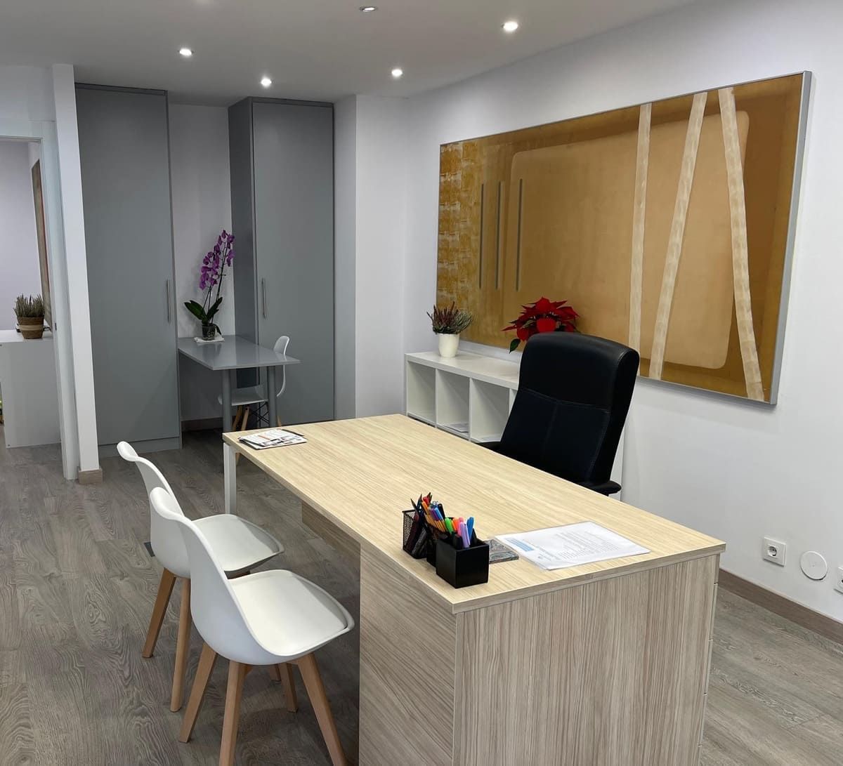 Una oficina con escritorio, sillas y arte abstracto en la pared. El escritorio es de madera clara.