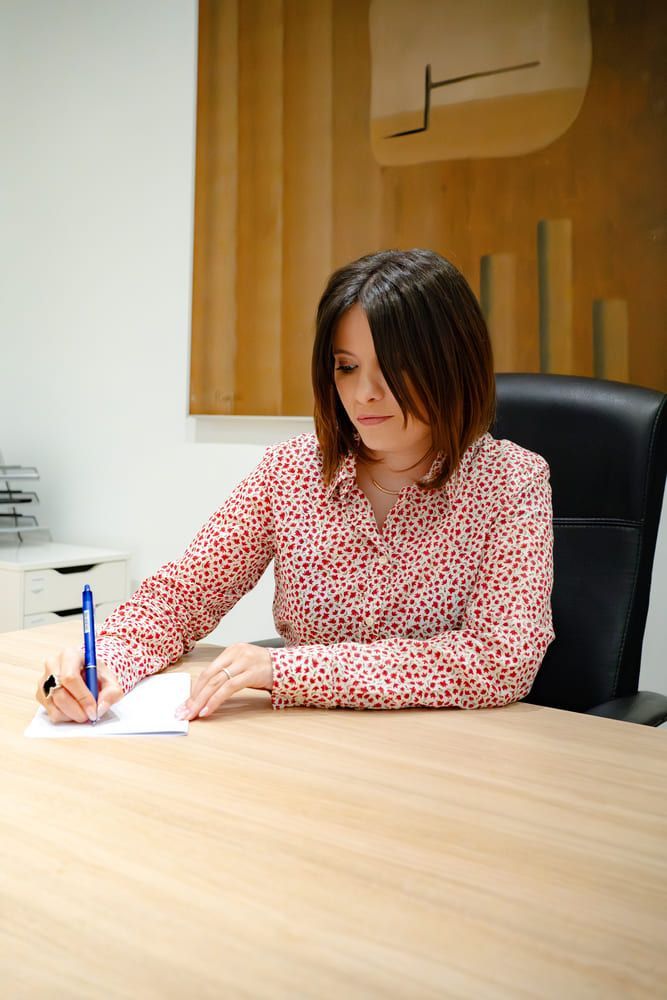Mujer con camisa estampada escribiendo en un escritorio, en un entorno de oficina.