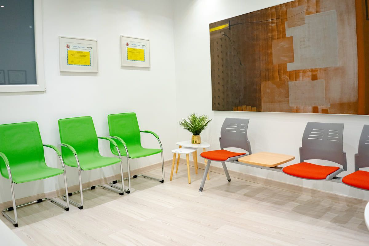 Sala de espera con sillas verdes y grises, paredes blancas y arte abstracto.