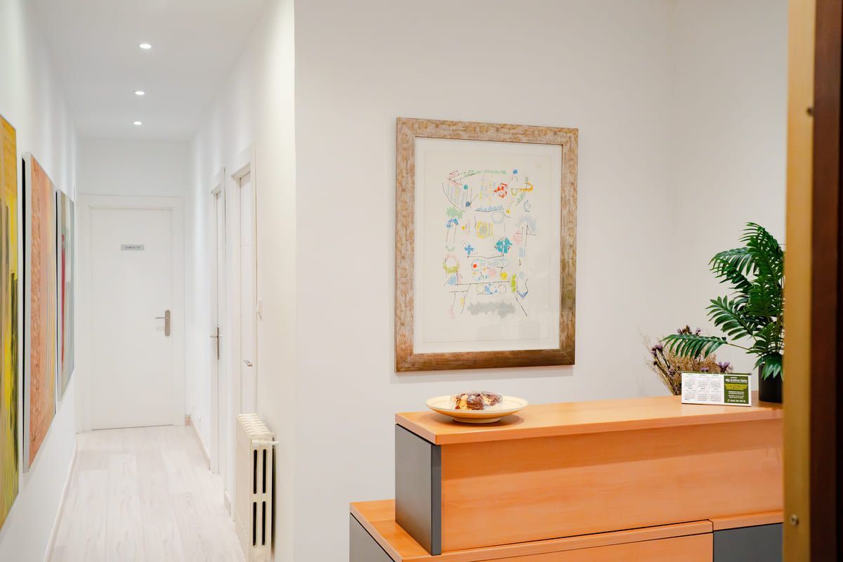 Pasillo con mostrador de recepción, obras de arte y una planta en un espacio de oficina de tonos neutros.