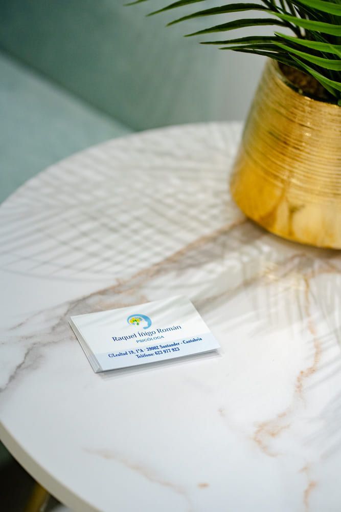 Tarjeta de visita sobre una mesa de mármol junto a un jarrón dorado con una planta verde.