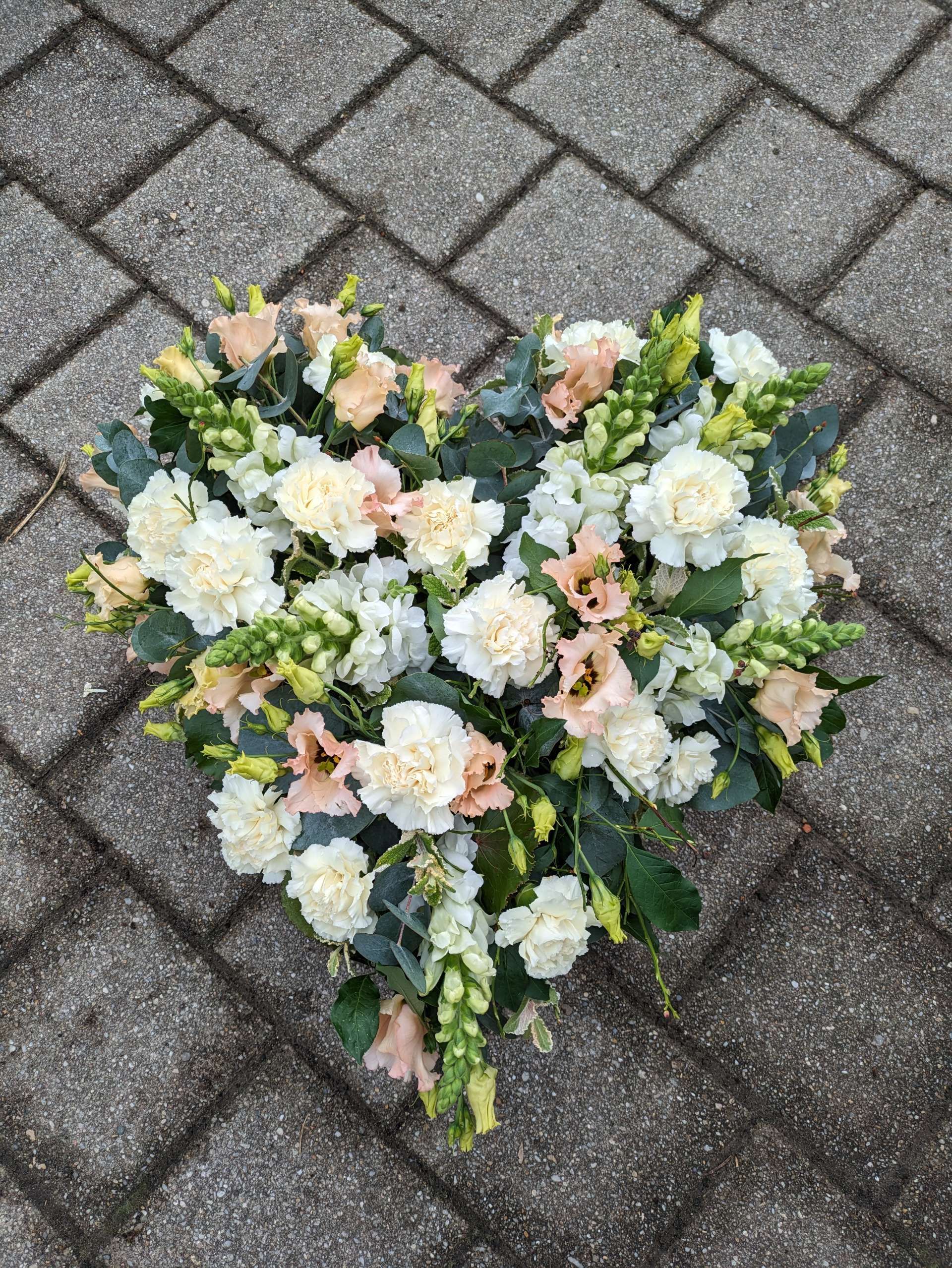 Breit gebundener Herz-Blumenstrauß mit hellen Blüten auf Pflastersteinen